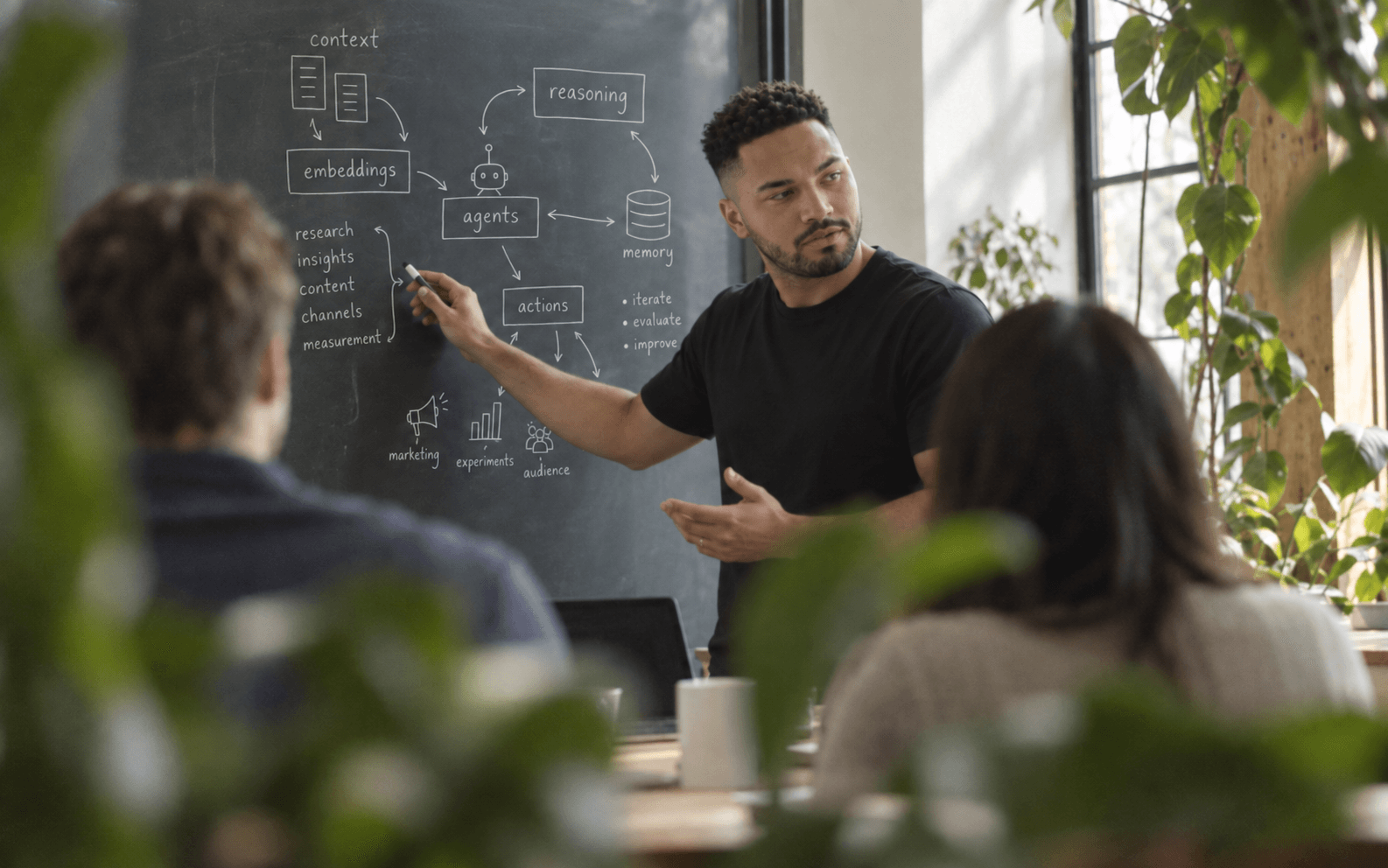 A team member maps an agent workflow on a chalkboard while colleagues listen